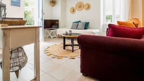 A living room with a TV, sofa, and a dining area with a table and chairs. - Charming Stone Cottage with Heated Pool, Private Garden, and Close to Beaches (Saint-Lyphard)