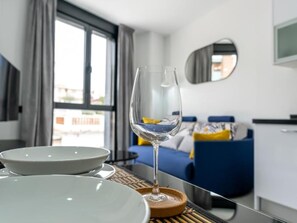 Hotelkamer met een eettafel, gedekt met borden en een wijnglas, een bed met blauw beddengoed en uitzicht buiten door een raam.