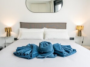 Een net opgemaakt bed met twee kussens, een grote spiegel erboven en twee nachtlampjes aan weerszijden.