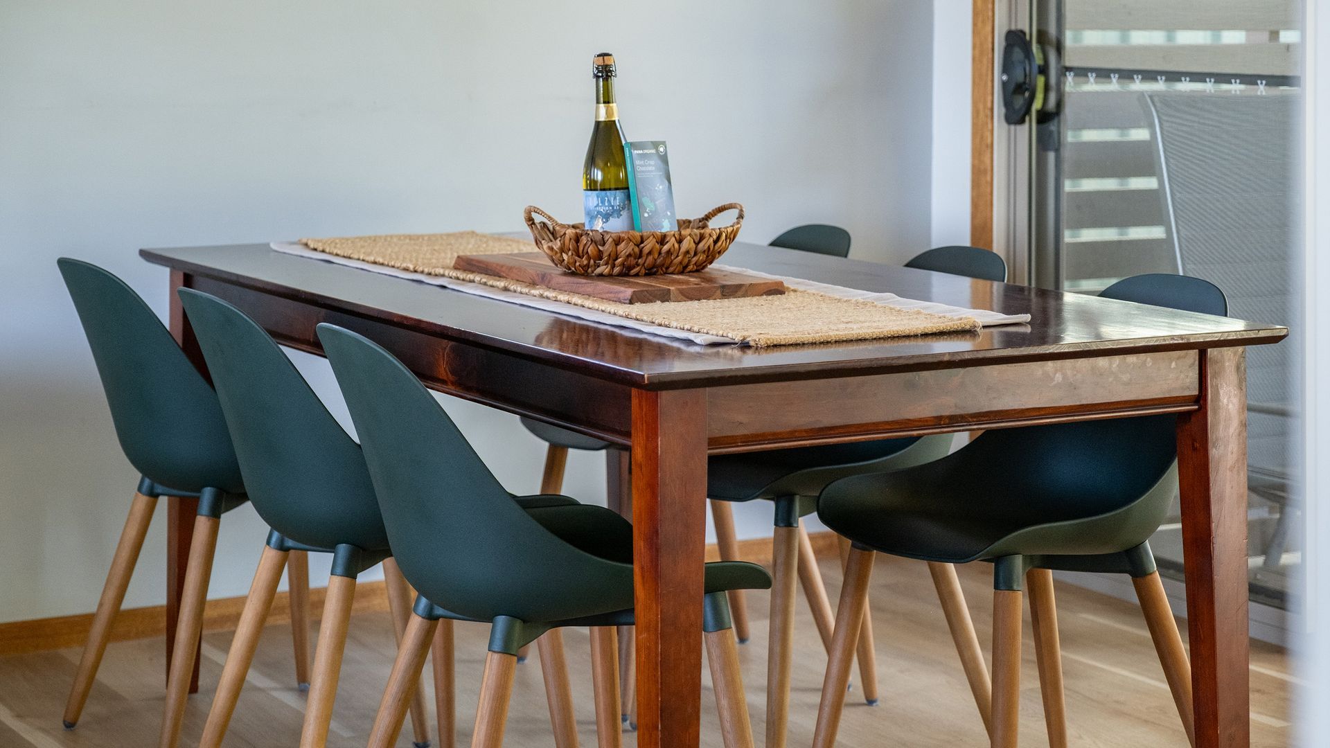 A dining table with a bottle of wine and a box, surrounded by chairs.