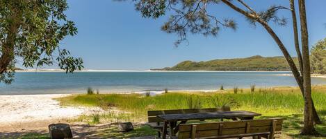 Ein Strand mit einer Holzbank und einem Picknicktisch, freier Blick auf das Meer und eine entfernte Hügelkette.