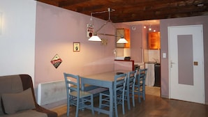A cozy dining area with a wooden ceiling, a table with blue chairs, and a kitchenette in the background. - Cozy 2-Bedroom Apartment for 6 with Mountain View, Balcony, and Ski-in/Ski-out Access (Les Orres)