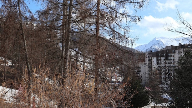 A mountainous landscape with snow-covered peaks, a building with multiple balconies, and a forested area with bare trees. - Cozy 2-Bedroom Apartment for 6 with Mountain View, Balcony, and Ski-in/Ski-out Access (Les Orres)
