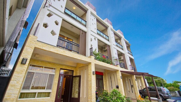 A multi-story building with balconies, a covered entrance, and a parked car. - Kuan-Pin B&B (Wujie)