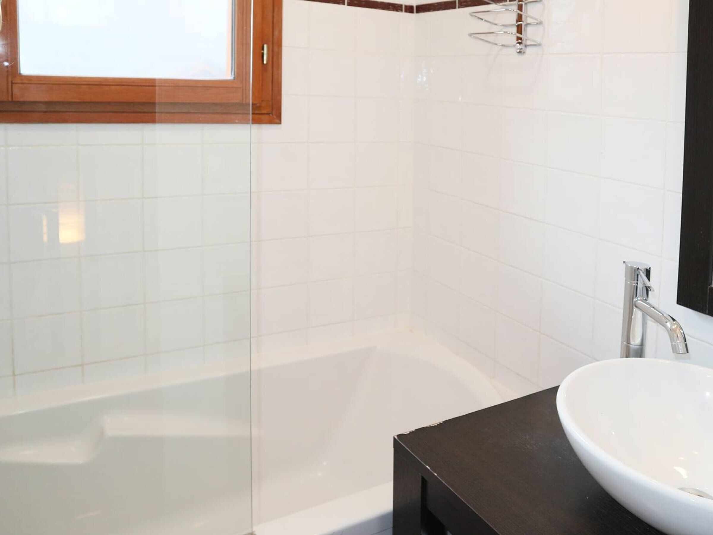 A bathroom with a glass shower enclosure, a white bathtub, and a black countertop with a white sink.