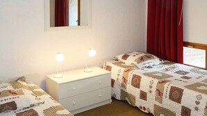 Une chambre avec deux lits, une commode blanche, un miroir et des rideaux rouges.