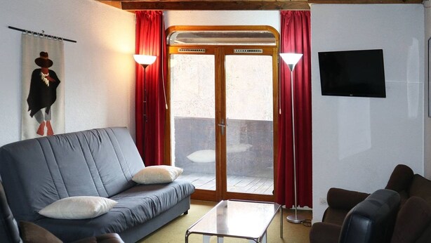 Un salon avec un canapé gris, un fauteuil noir, une table basse et un téléviseur fixé au mur.