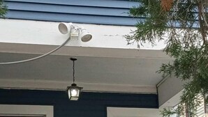 Un porche avec une porte rouge, un mur recouvert de bardage bleu, une chaise noire et un luminaire suspendu.