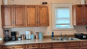 Une cuisine avec des meubles de rangement en bois, un plan de travail équipé de divers appareils et une fenêtre avec des stores.