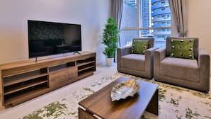 A modern living room with a flat-screen TV on a wooden stand, two grey armchairs with patterned cushions, a potted plant, and a decorative leaf on a wooden coffee table. - Apartment Downtown Dubai Near Burj Khalifa (Dubai)