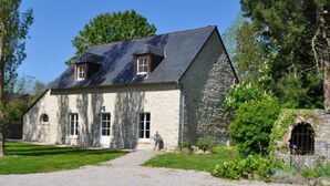 A stone building with a gravel driveway, a small garden, and a stone wall with a window.