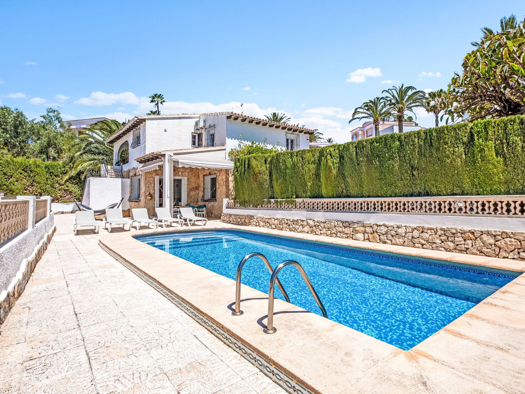 A pool area with a stone deck, lounge chairs, and a white building with a stone facade.