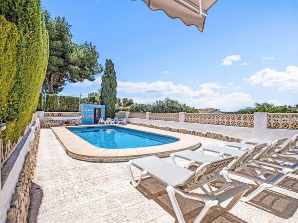 Une piscine avec des chaises longues, un chemin de pierre et une porte bleue.