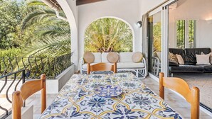 A balcony with a tiled table, two white cushioned chairs, and a black sofa with cushions. - Vacation home Adinga by Interhome (Moraira)