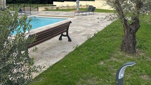 En swimmingpool med en bænk, omgivet af græs og træer.