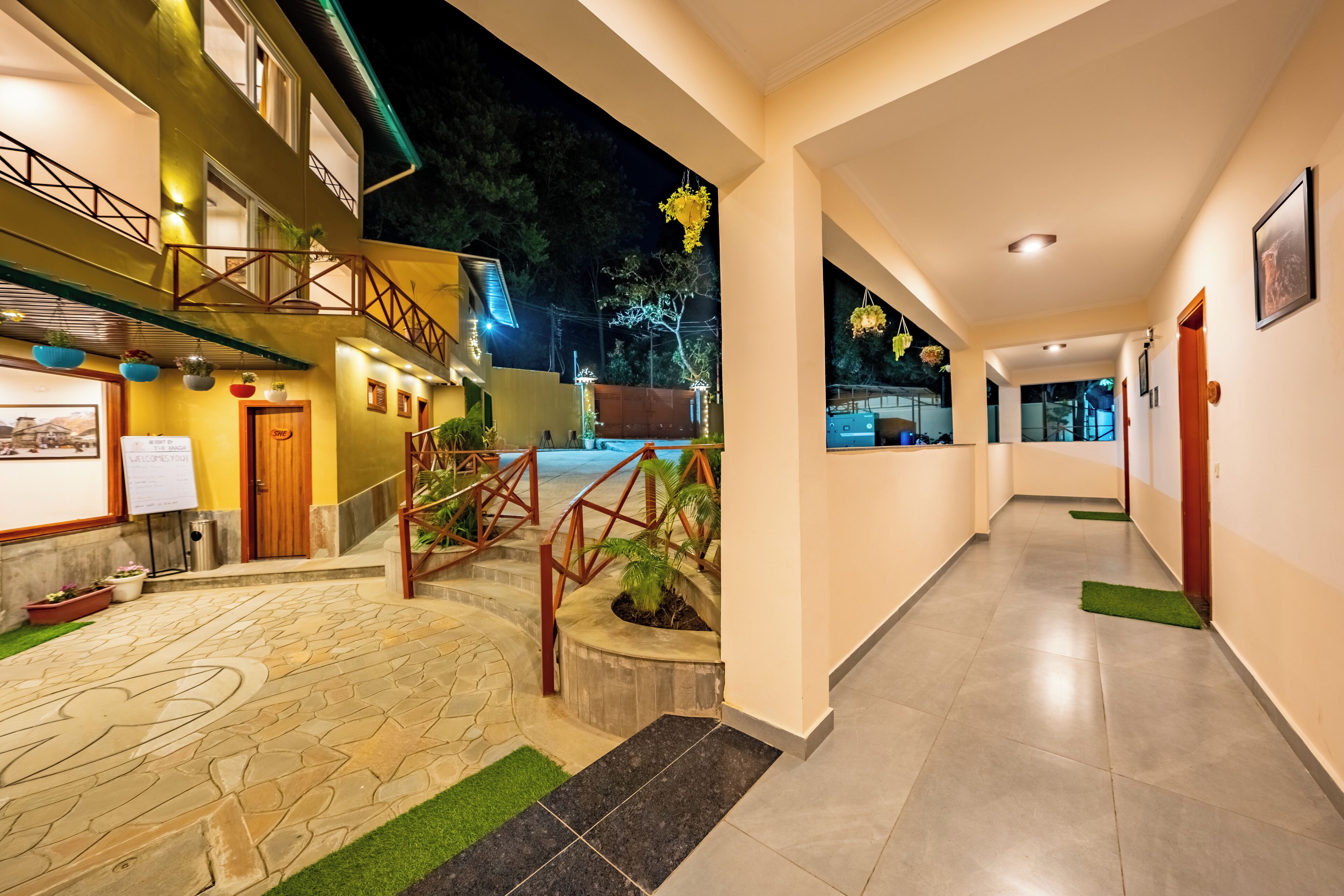 A hotel corridor with a stone-tiled floor, a staircase with wooden railings, and a balcony with potted plants.