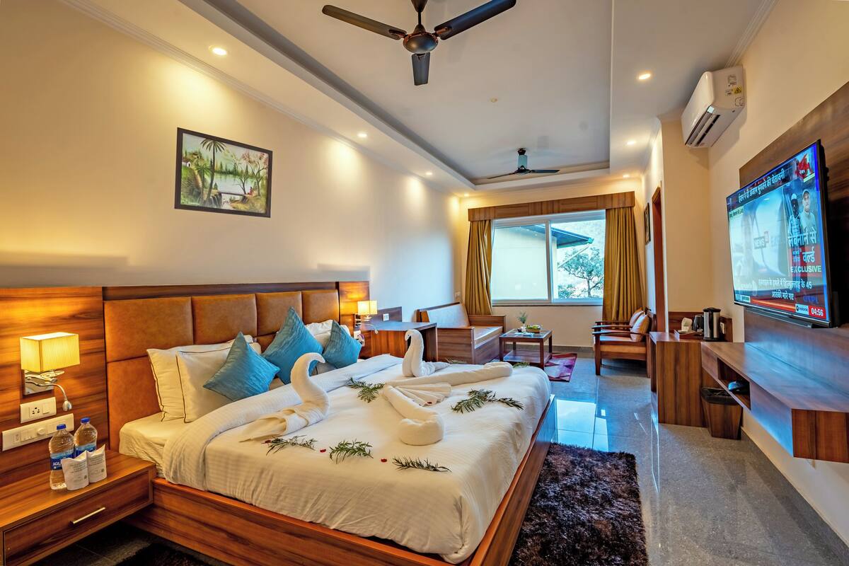 A hotel room with a large bed, a TV, a desk, and a window with curtains.