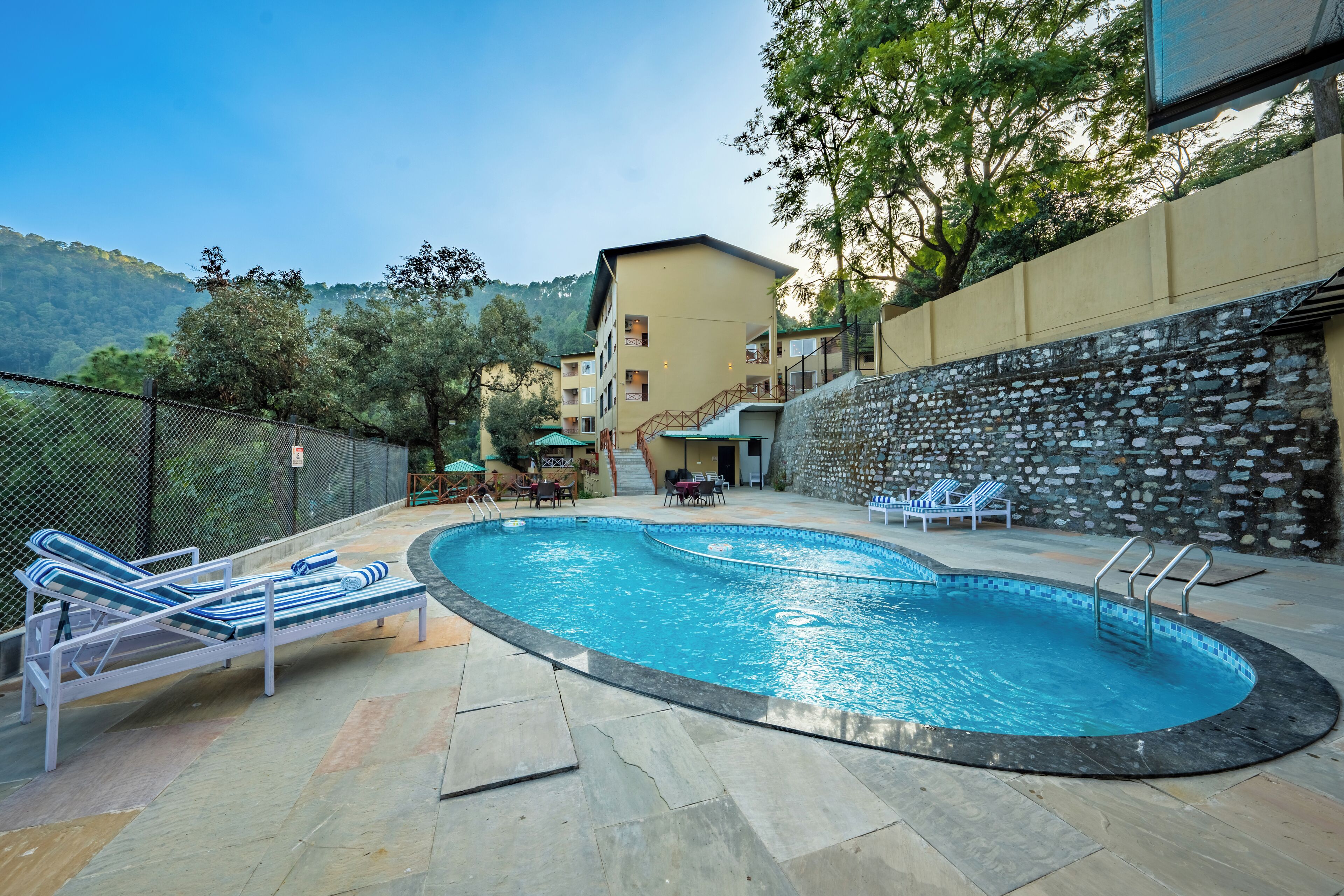 A swimming pool with lounge chairs, a stone wall, and a view of a mountainous area.