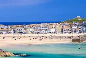 A coastal town with a sandy beach, boats, and buildings along the shore.
