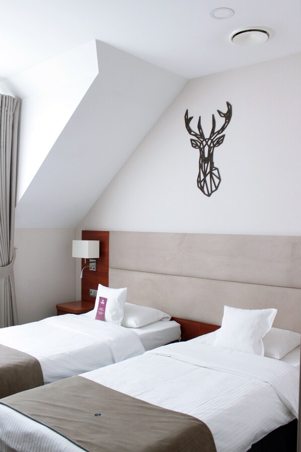 A hotel room with two beds, a wooden headboard, a wall-mounted deer head decoration, a bedside table with a lamp, and a window with curtains. - ParkHotel Lyson (Andrychow)