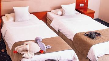 A hotel room with two beds, a nightstand with a lamp, a suitcase, and a stuffed toy on one bed.