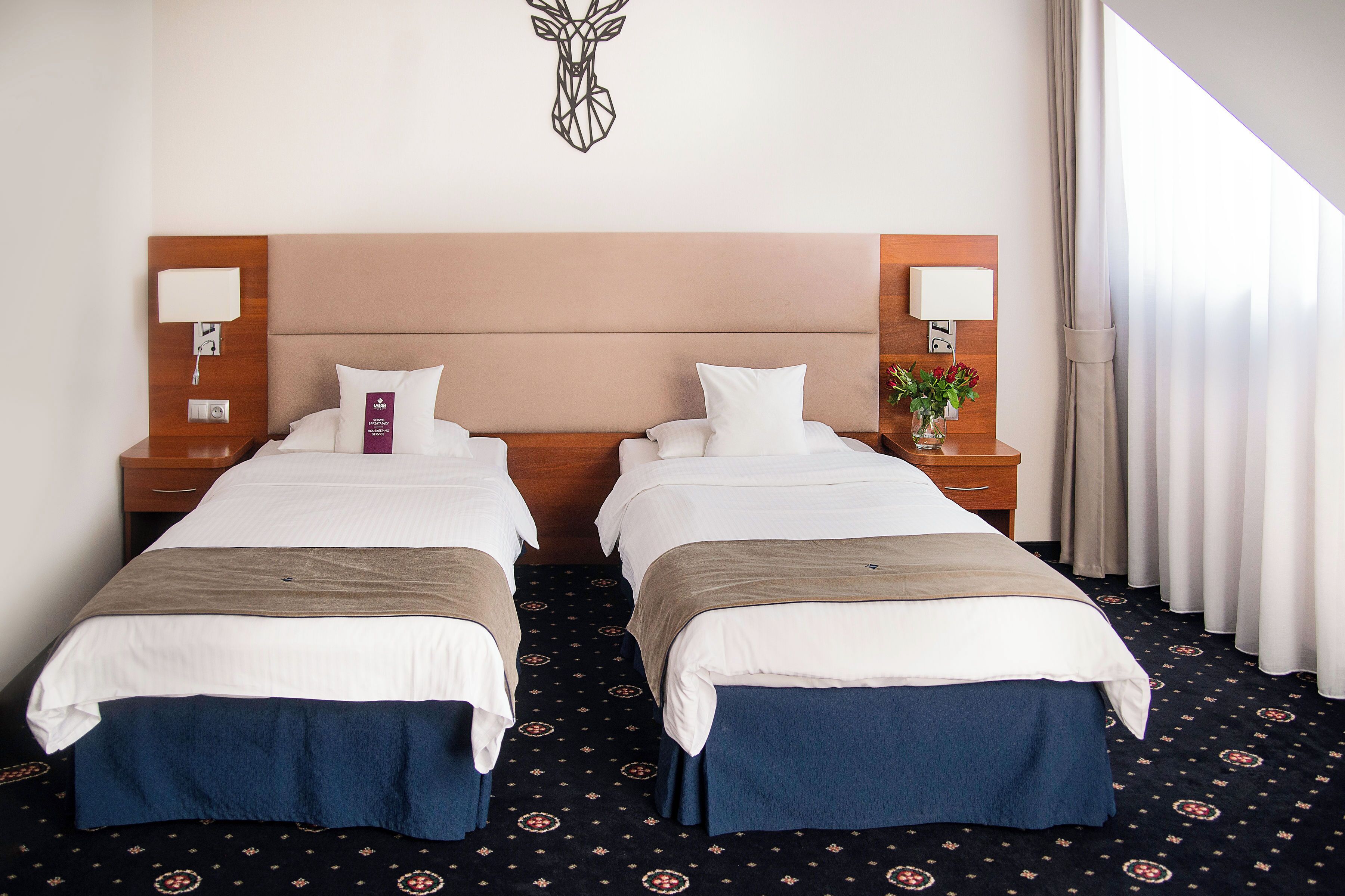Una habitación de hotel con dos camas, cabecero de madera, mesitas de noche con lámparas, una obra de arte colgada en la pared y una alfombra estampada.