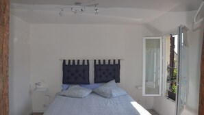 Een slaapkamer met een bed, nachtkastje, raam met uitzicht en een plafondlamp.
