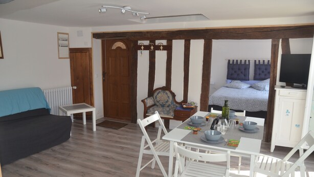 Een kamer met een bed, een televisie, een eettafel met stoelen, een bank en een raam met houten kader.