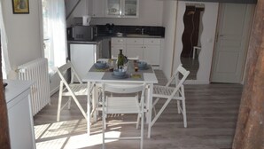 Een compacte keuken met witte kastjes, een eettafel met vier stoelen en een klein schiereiland met een spoelbak.