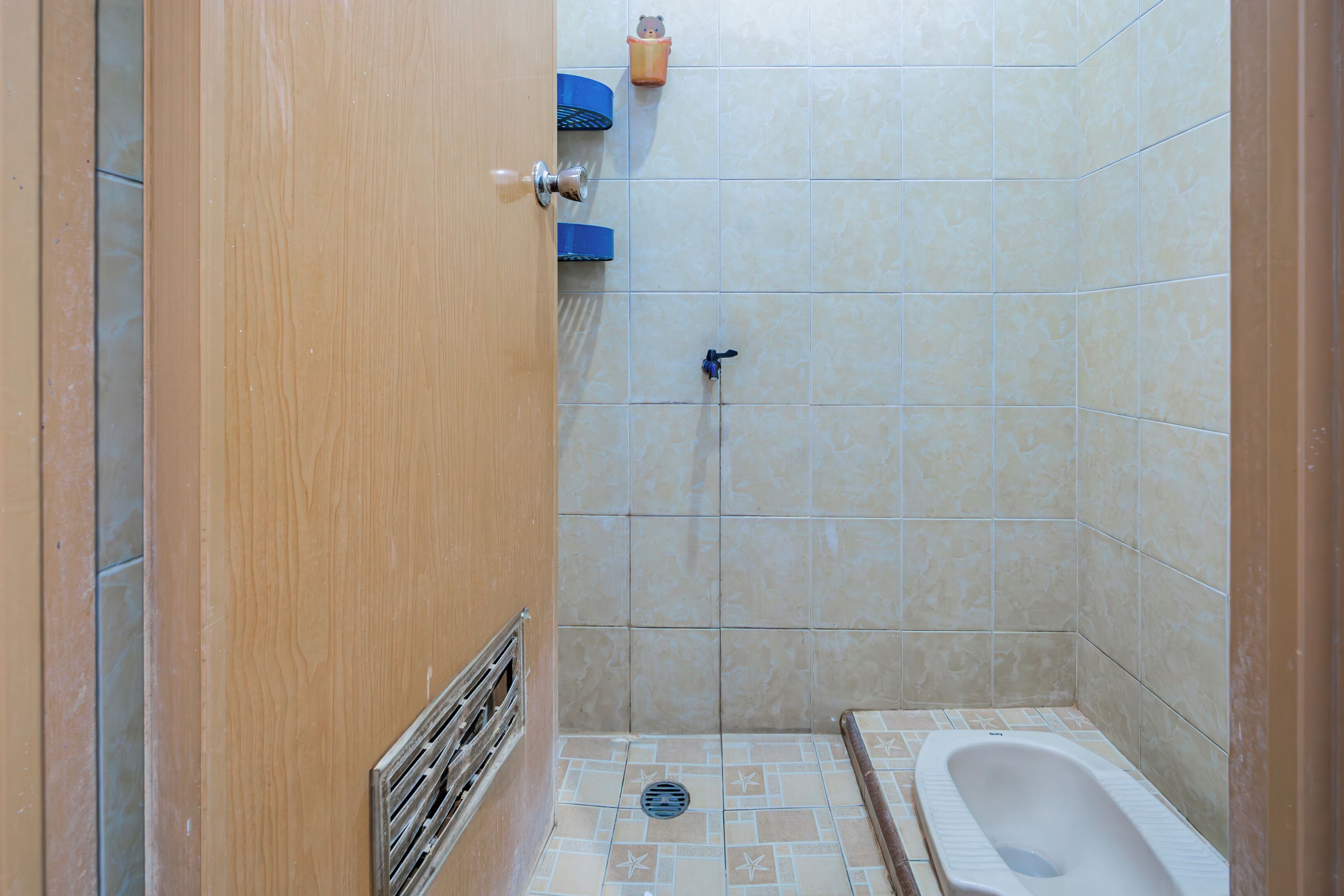 A small, tiled bathroom with a wooden door, a toilet, and a shower area.