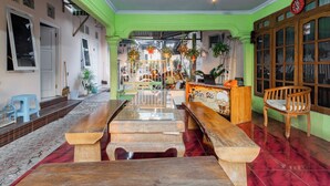 A spacious room with a long wooden table, a bench, and a wooden chair. There is a small stool and a potted plant on the table. - Hotel O Maluku Guest House (Blitar)