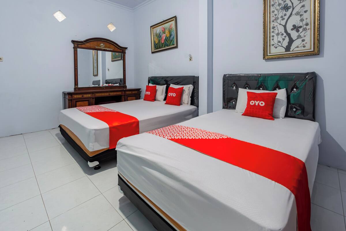 A hotel room with two beds, each with a red and white bedspread, a large mirror, and a painting on the wall.