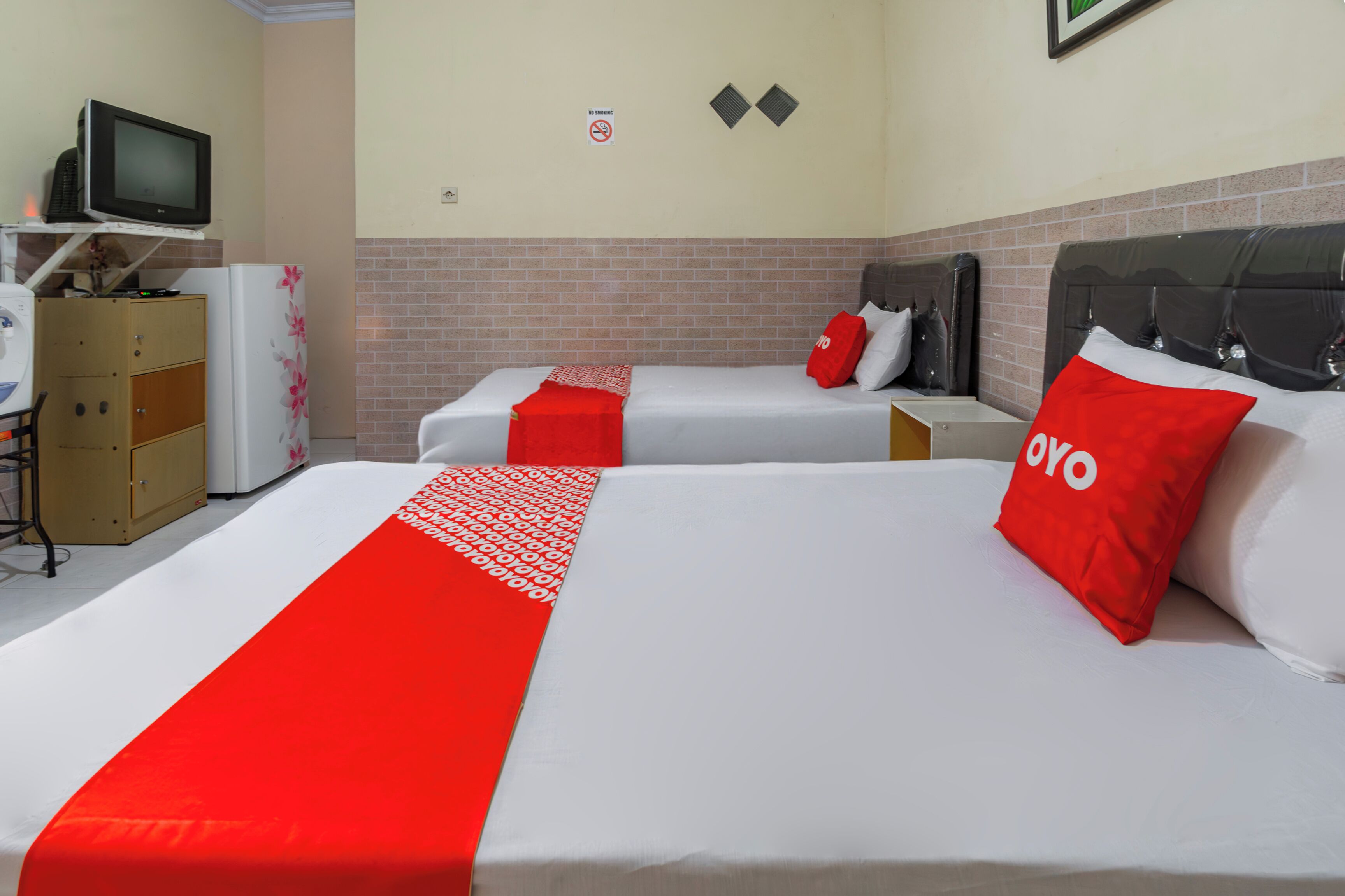 A hotel room with two beds, a television on a stand, a refrigerator, and a cabinet.