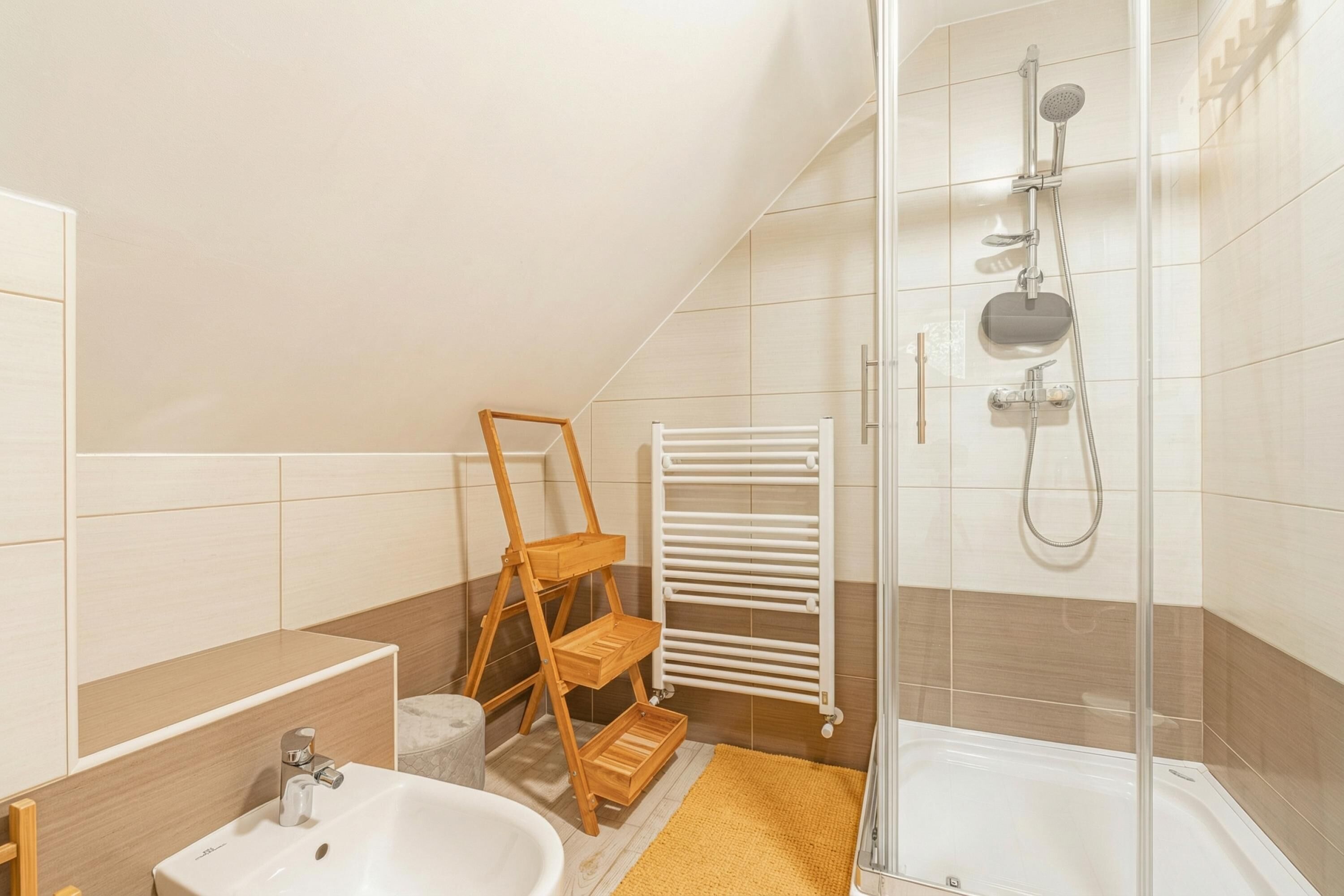 Une salle de bain moderne avec une douche, un lavabo, une étagère en bois et un porte-serviettes blanc.