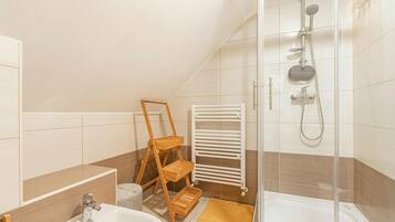 Une salle de bain moderne avec une douche, un lavabo, une étagère en bois et un porte-serviettes blanc.