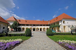 A courtyard with a cobblestone path, arches, and a building with a red roof.