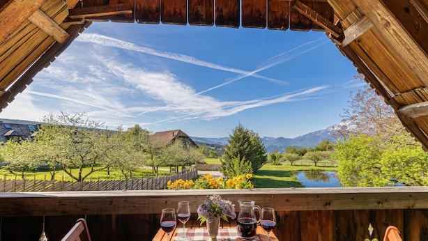 A wooden table with a cheese platter, wine glasses, and a pitcher, set against a scenic mountain view. - Suite Alder embraced by nature (Prevalje)