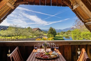 A wooden table with a cheese platter, wine glasses, and a pitcher, set against a scenic mountain view. - Suite Alder embraced by nature (Prevalje)
