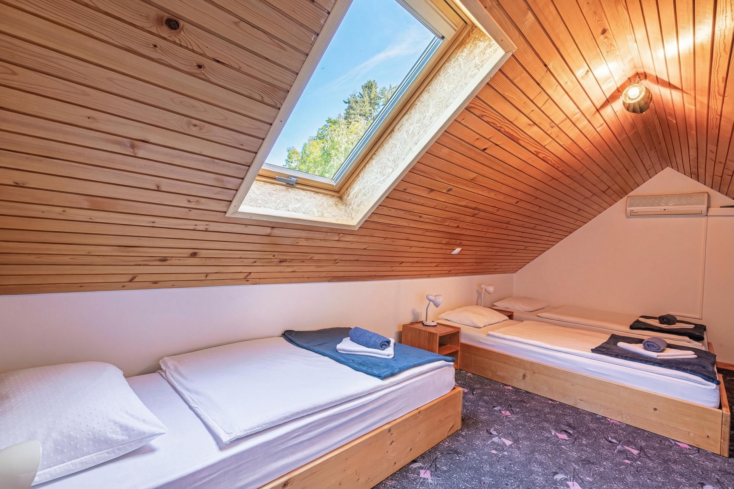 Una habitació petita i acollidora amb parets de fusta i sostre inclinat, amb dos llits i un fanal.