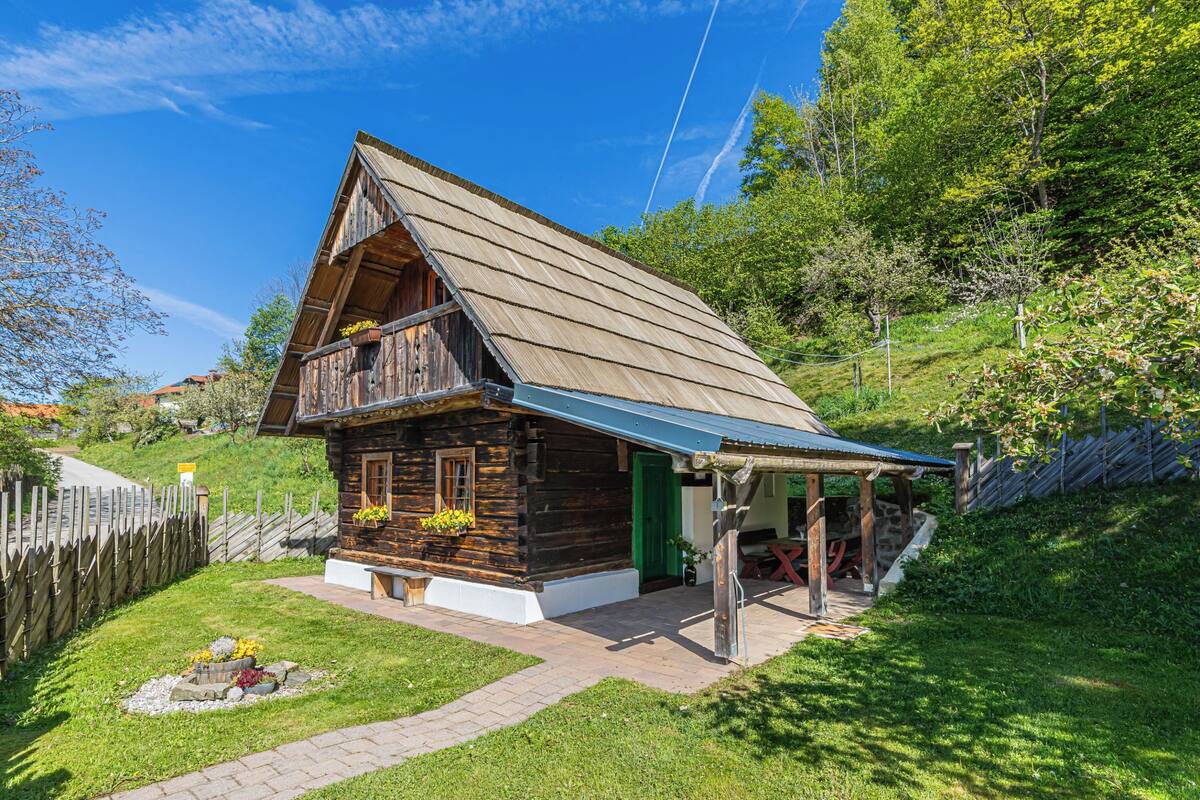 Une cabane en bois avec un toit en pente, une véranda et un petit jardin agrémenté de fleurs.