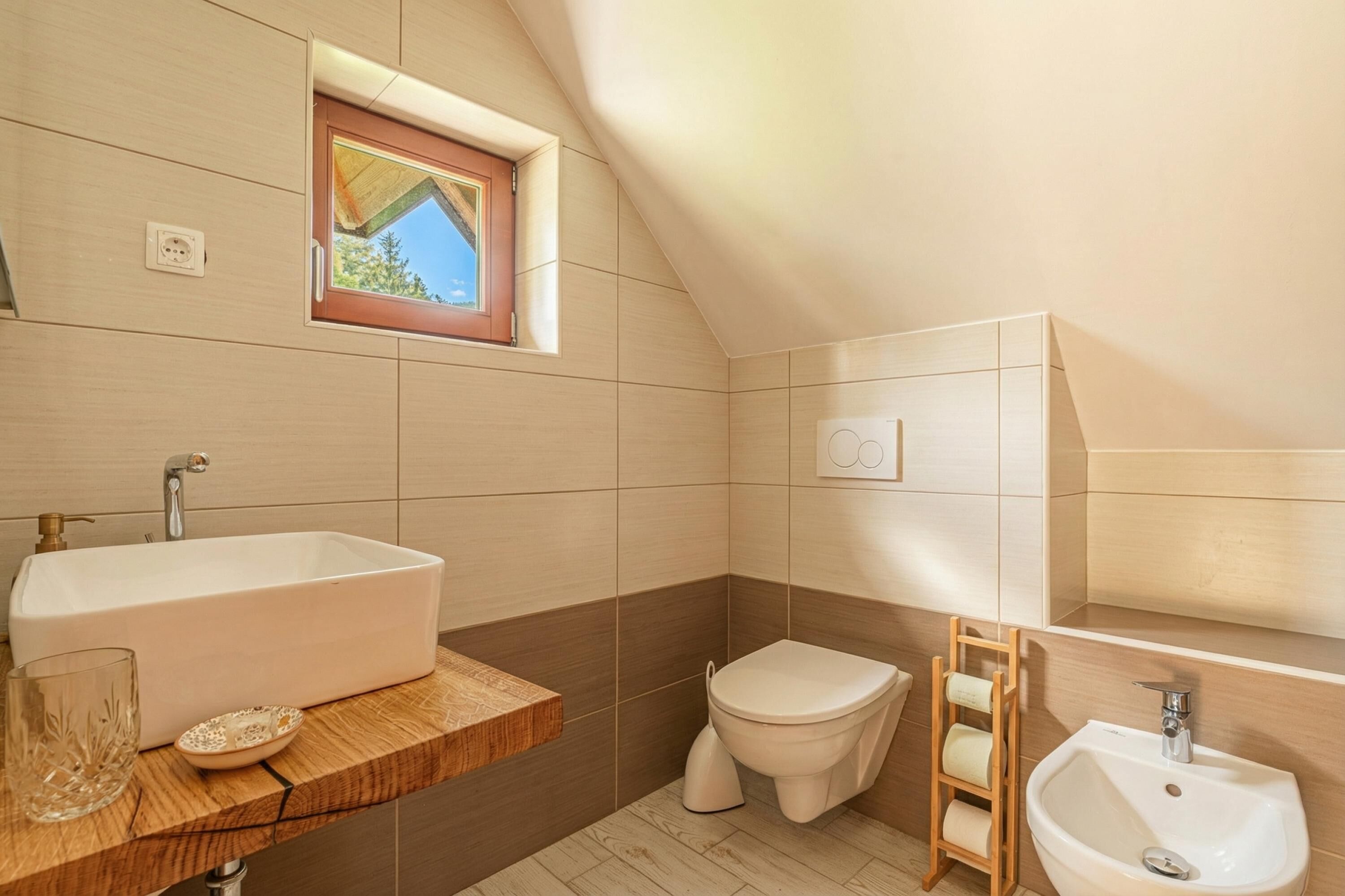 A bathroom with a bathtub, toilet, and sink, wooden countertop, and a window.
