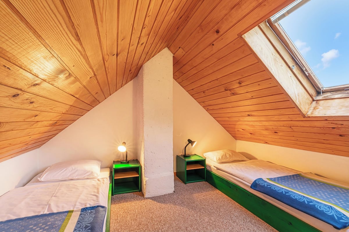 Une petite chambre mansardée avec deux lits, un plafond avec des lattes en bois et un puits de lumière.
