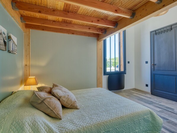 A bedroom with a wooden ceiling, a bed with a quilt, a window, and a door.