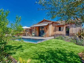 A wooden house with a swimming pool, surrounded by a well-maintained lawn and various plants.