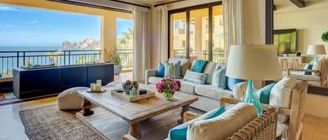 Un salón amplio con un gran ventanal que ofrece vistas al océano, un conjunto de sofás, una mesa de centro y un televisor.