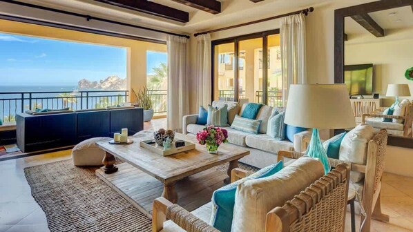 A spacious living room with a large window offering a view of the ocean, a sofa set, a coffee table, and a television.