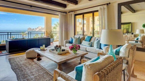 Ein geräumiges Wohnzimmer mit großem Fenster zum Meer, einer Sofagarnitur, einem Couchtisch und einem Fernseher.