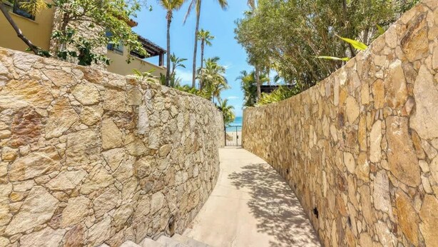 A stone pathway leading to a beach, flanked by palm trees and a building with a yellow facade. - Hacienda Beach Club Residence Amazing View! (Cabo San Lucas)