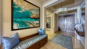 A modern interior with a large abstract painting, a bench with cushions, a wooden door, and a hanging light fixture. - Hacienda Beach Club Residence Amazing View! (Cabo San Lucas)