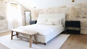 Een slaapkamer met een groot bed, een nachtkastje, een hanglamp en een stenen muur.